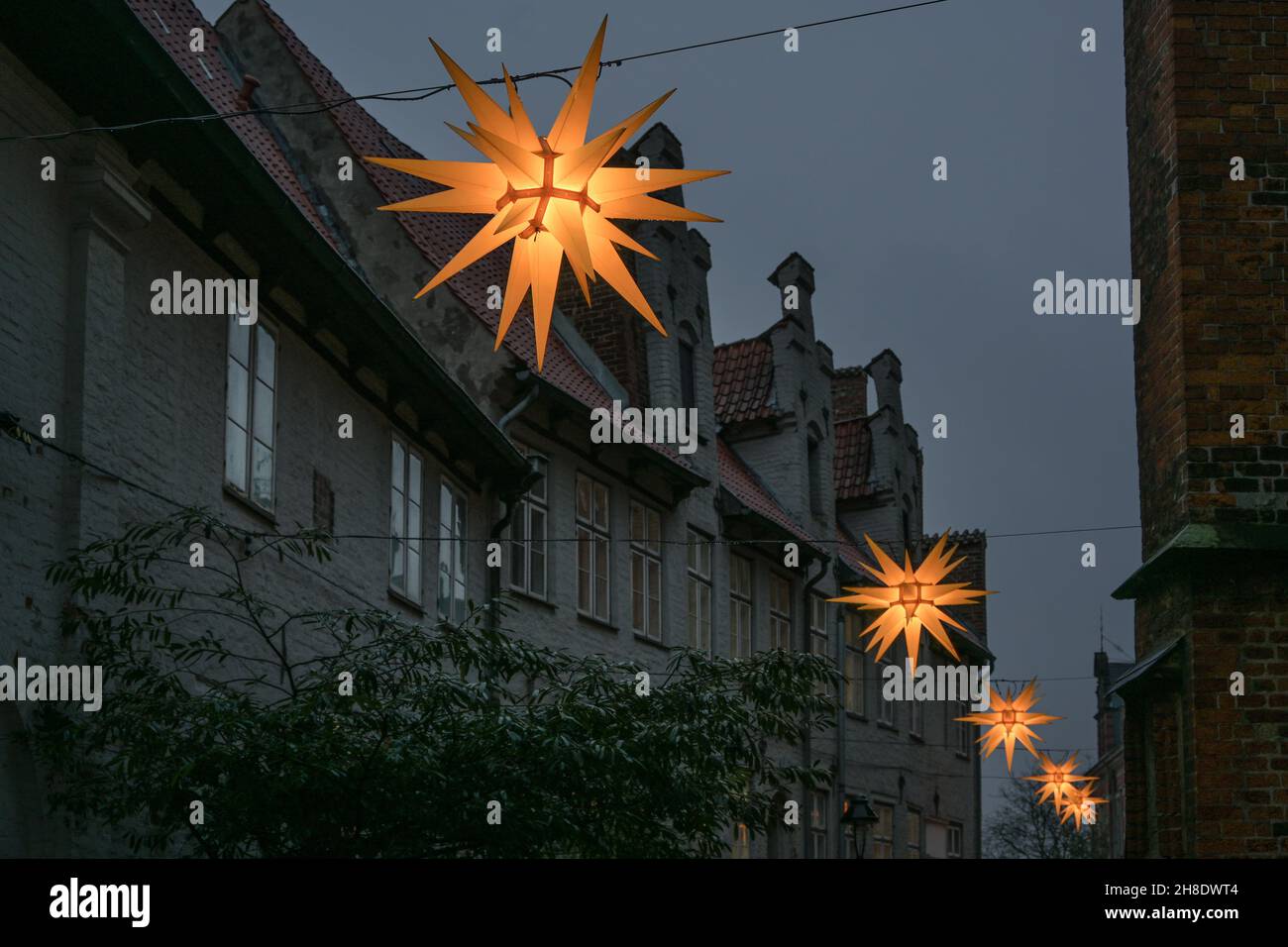 Fila di stelle moravi scintillanti tra le case storiche nella città vecchia di Lubeck in Germania per l'avvento e il Natale di notte, spazio copia, selezionato foc Foto Stock