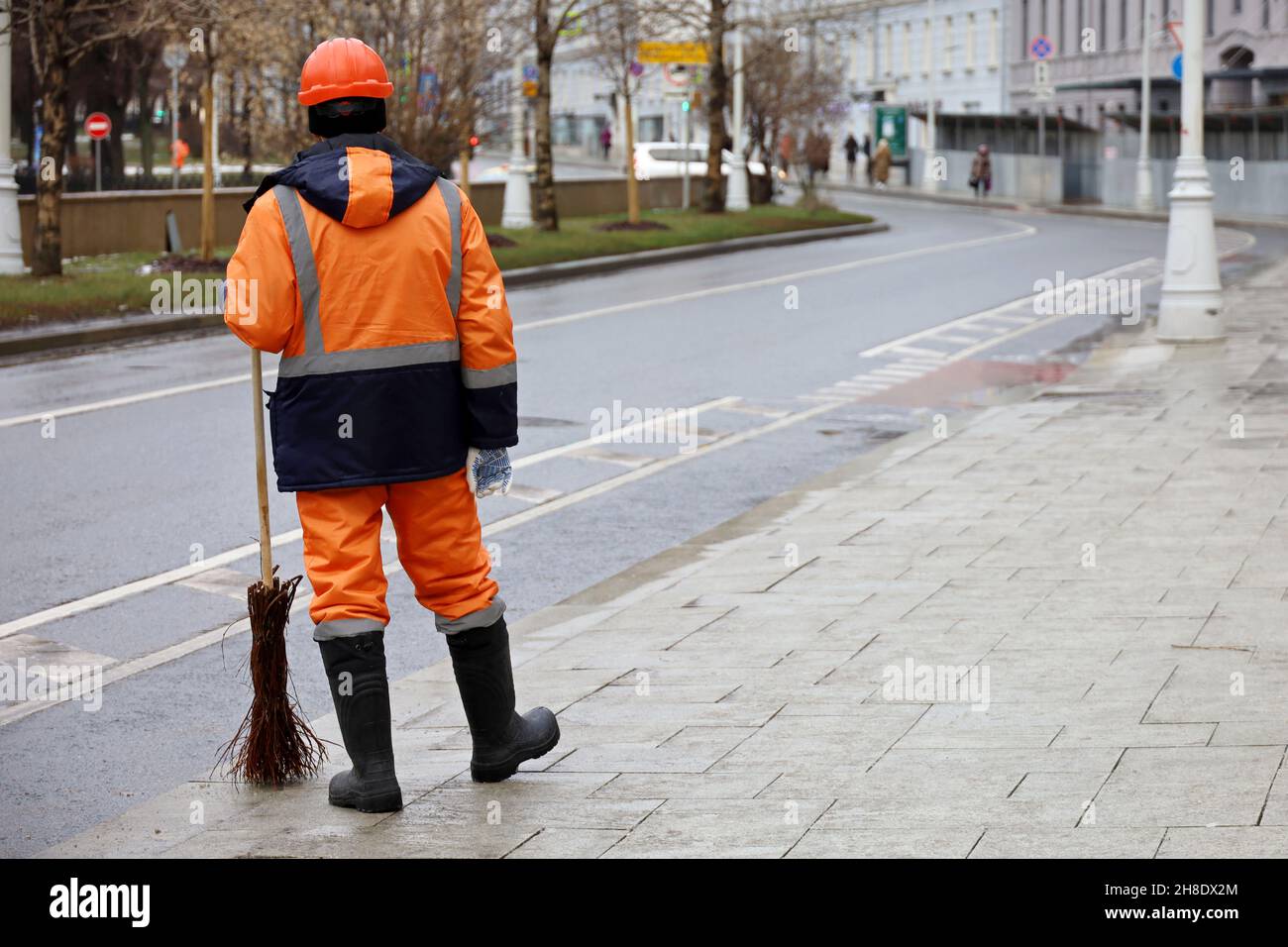 Janitor con scopa in città d'inverno, lavoratore comunale maschile in uniforme sul marciapiede. Pulizia di strada, concetto di lavoro non specializzato Foto Stock