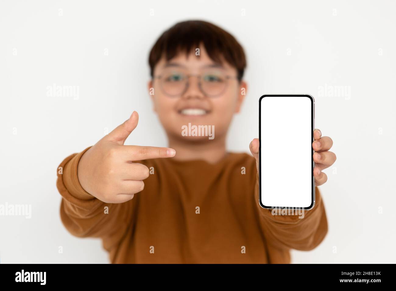 Chubby ragazzo asiatico puntando a smartphone con schermo vuoto, mockup Foto Stock