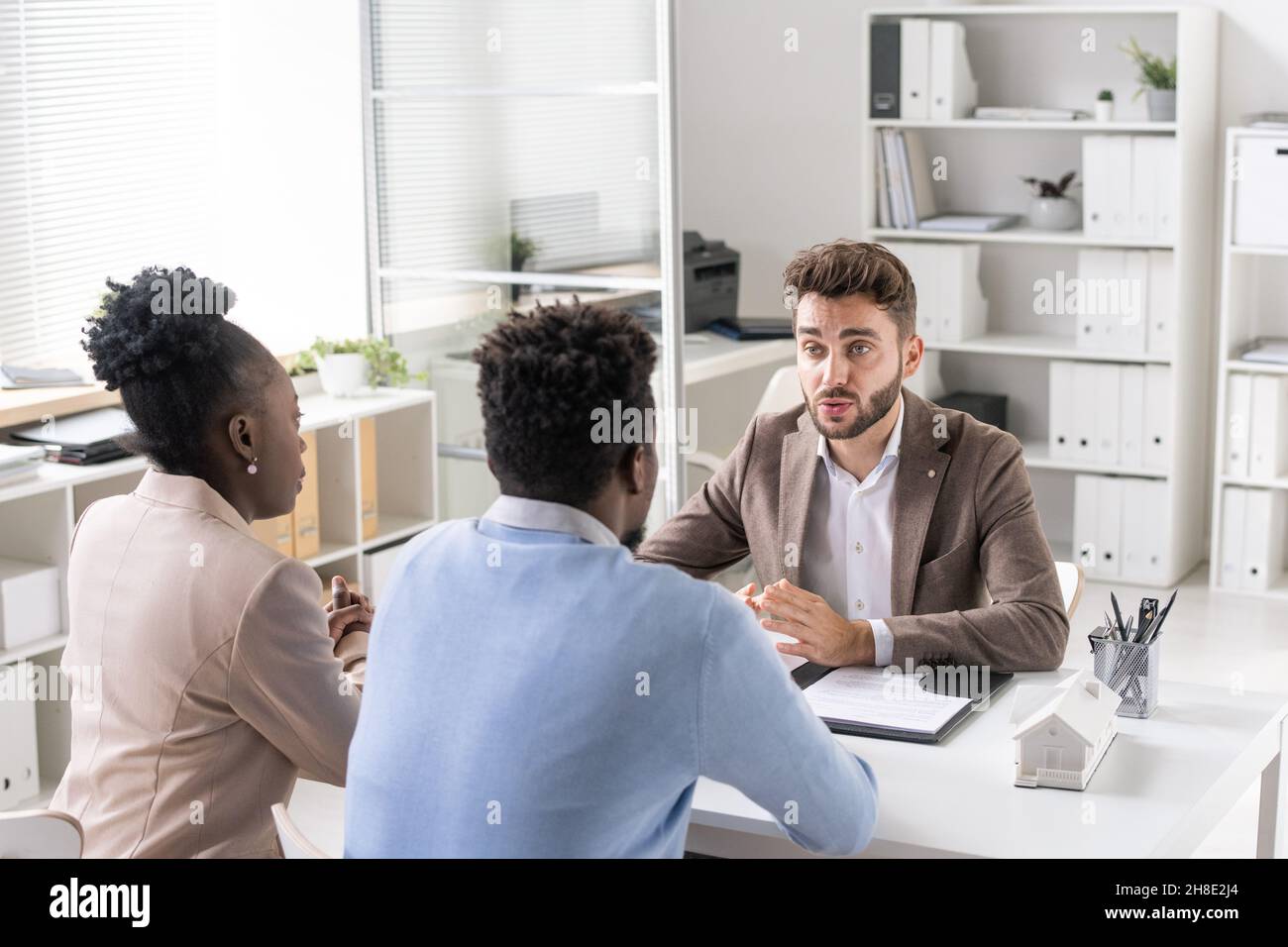 Giovane coppia afroamericana che ascolta il consulente finanziario barbato alla consultazione in carica Foto Stock