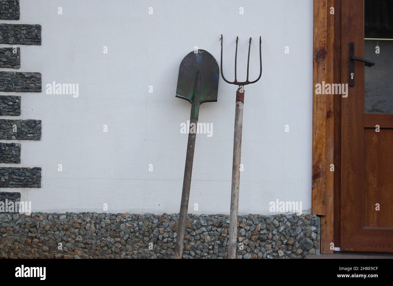 Attrezzo agricolo. Pitchfork e una pala stanno vicino al muro della casa. Foto Stock