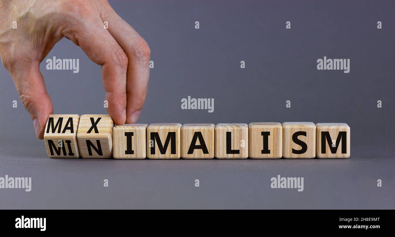 Simbolo del minimalismo o del massimalismo. L'uomo d'affari trasforma i cubi di legno e cambia la parola minimalismo in massimalismo. Bellissimo sfondo grigio. Business, mi Foto Stock