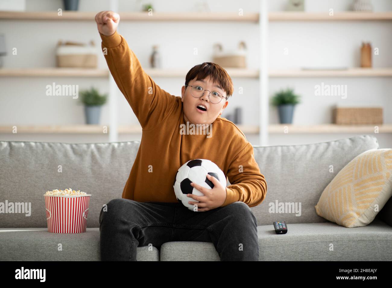 Ragazzo asiatico che guarda la partita di calcio a casa Foto Stock