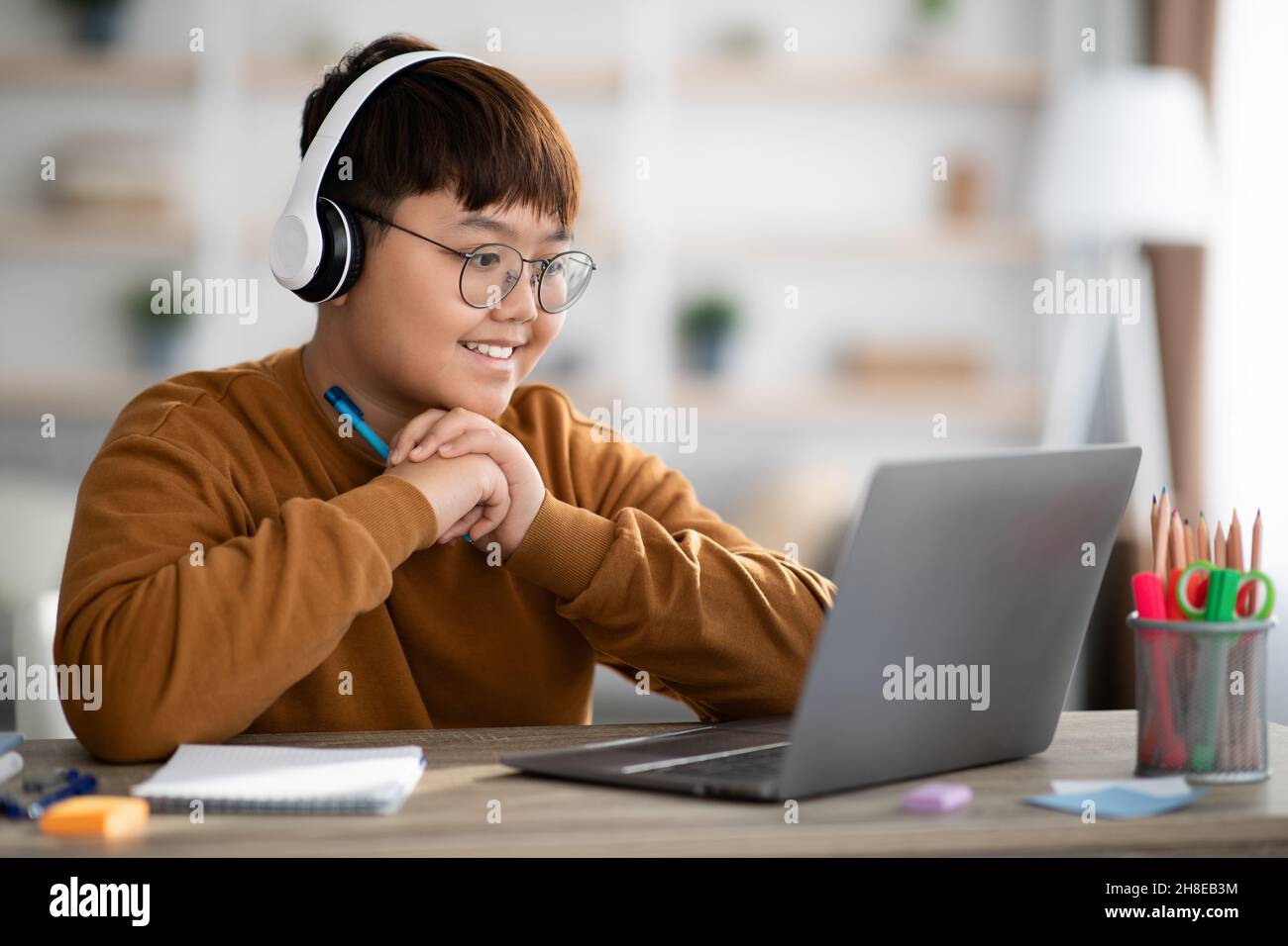 Cheerful ragazzo asiatico scuola che ha una lezione online da casa Foto Stock