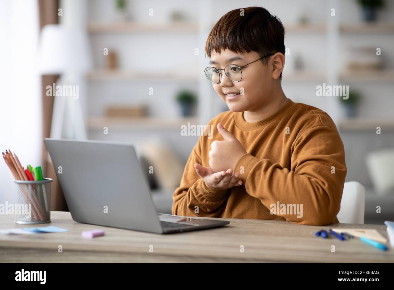 Ragazzo allegro seduto davanti al laptop, mostrando il pollice in su Foto Stock