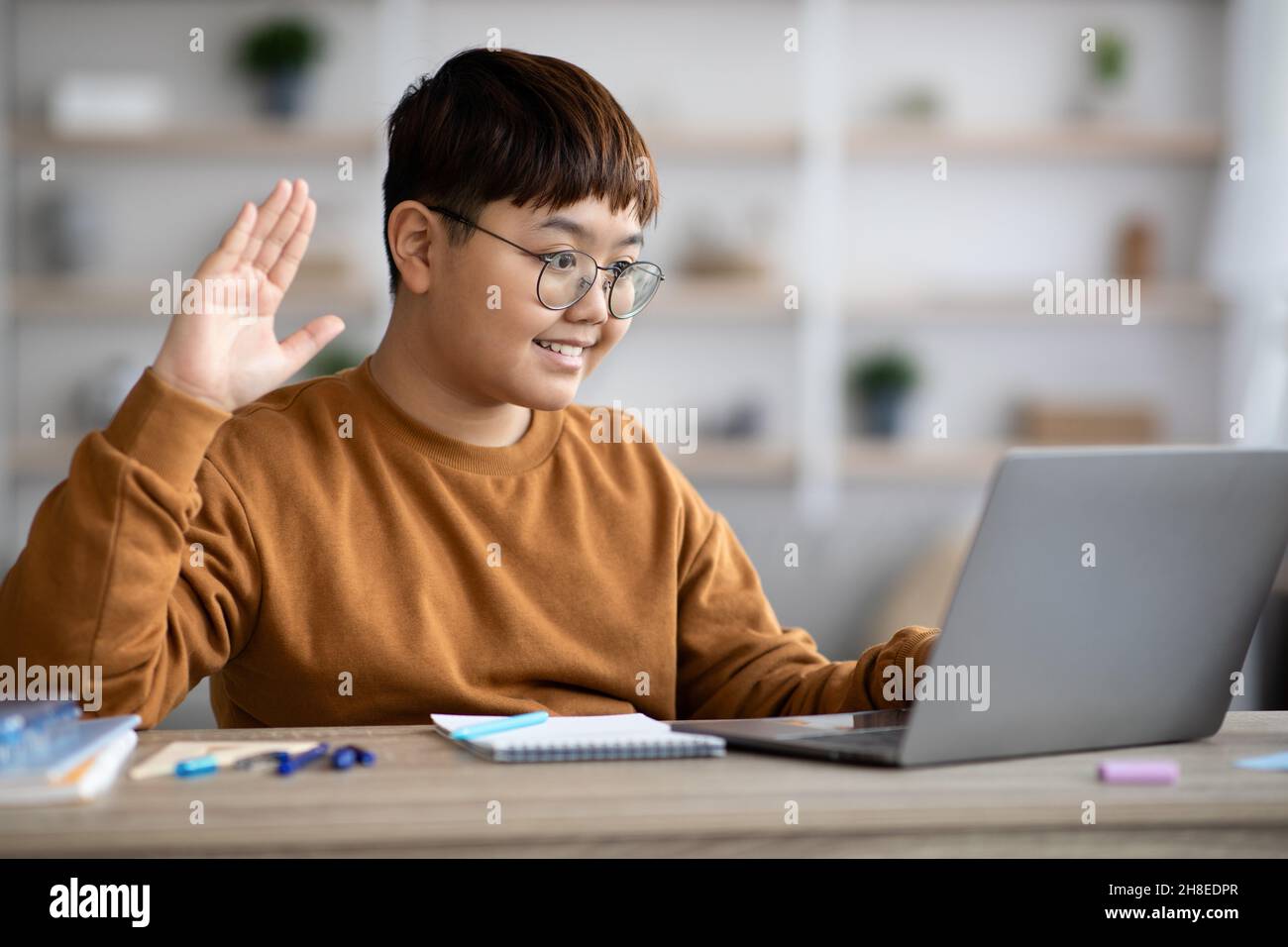 Sorridente ragazzo chubby coreano che agita sullo schermo del computer portatile Foto Stock