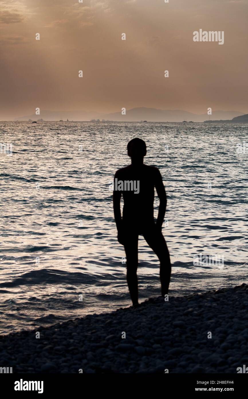 Arte contemporanea drammatica ritratto silhouette un uomo al mare in raggi del sole tramonto sullo sfondo onde scure e bello cielo sera Foto Stock