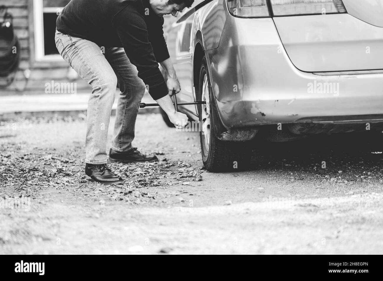 Scatto in scala di grigi di un maschio caucasico che cambia la ruota della vettura Foto Stock