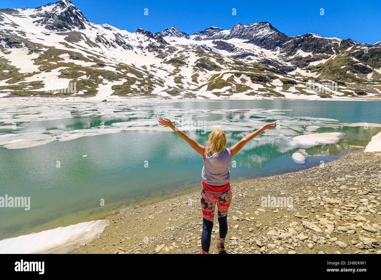 Donna a braccia aperte dopo un trekking sul lago bianco che si riflette con gli iceberg in Svizzera. Lungolago sul lago ghiacciato bianco nel Cantone di Grigioni al Foto Stock