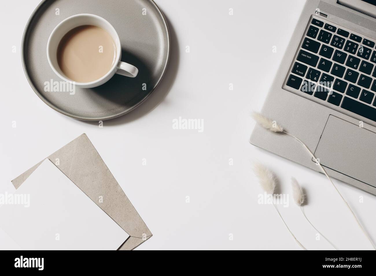 Composizione elegante dell'area di lavoro. Tazza di caffè, erba di laguru secca e portatile isolato su sfondo bianco tavolo. Mockup biglietto d'auguri vuoto con Foto Stock