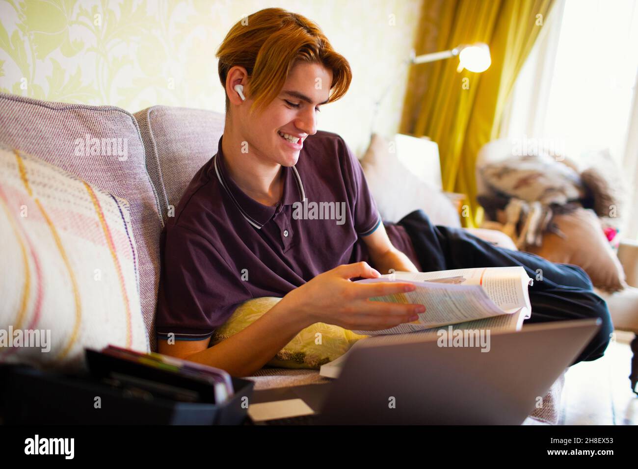 Ragazzo sorridente con libro di testo e laptop che studia a casa Foto Stock