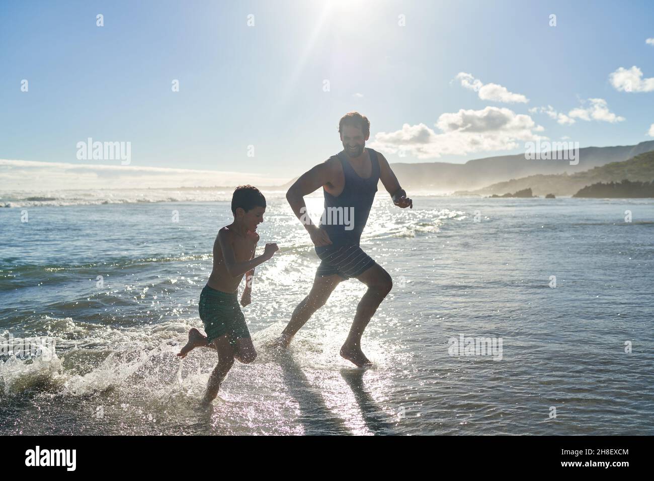 Felice padre e figlio che corre in mare soleggiato surf Foto Stock