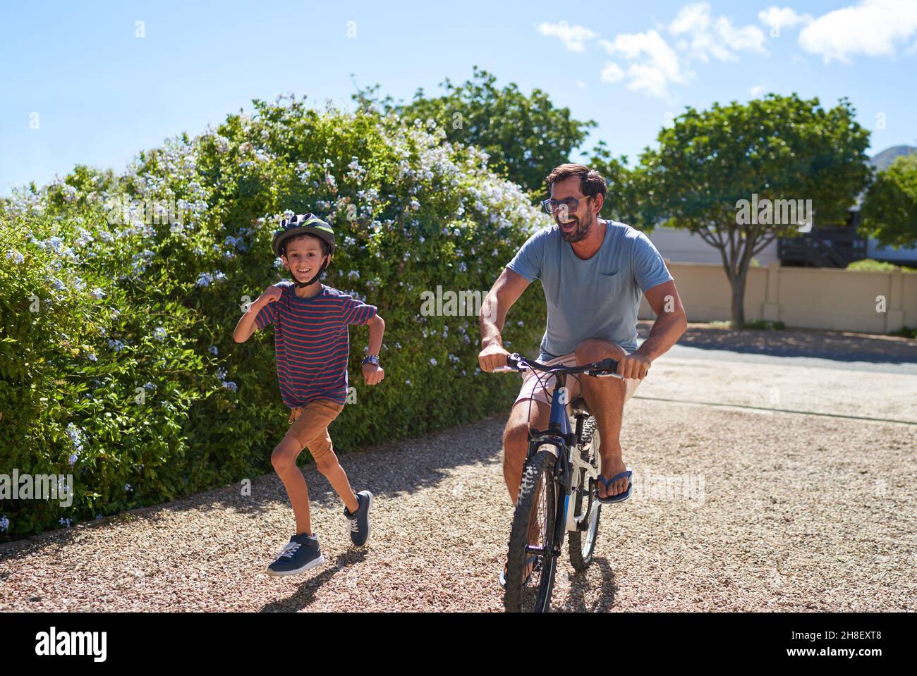 Felice padre e figlio correre e andare in bicicletta in un vialetto soleggiato Foto Stock