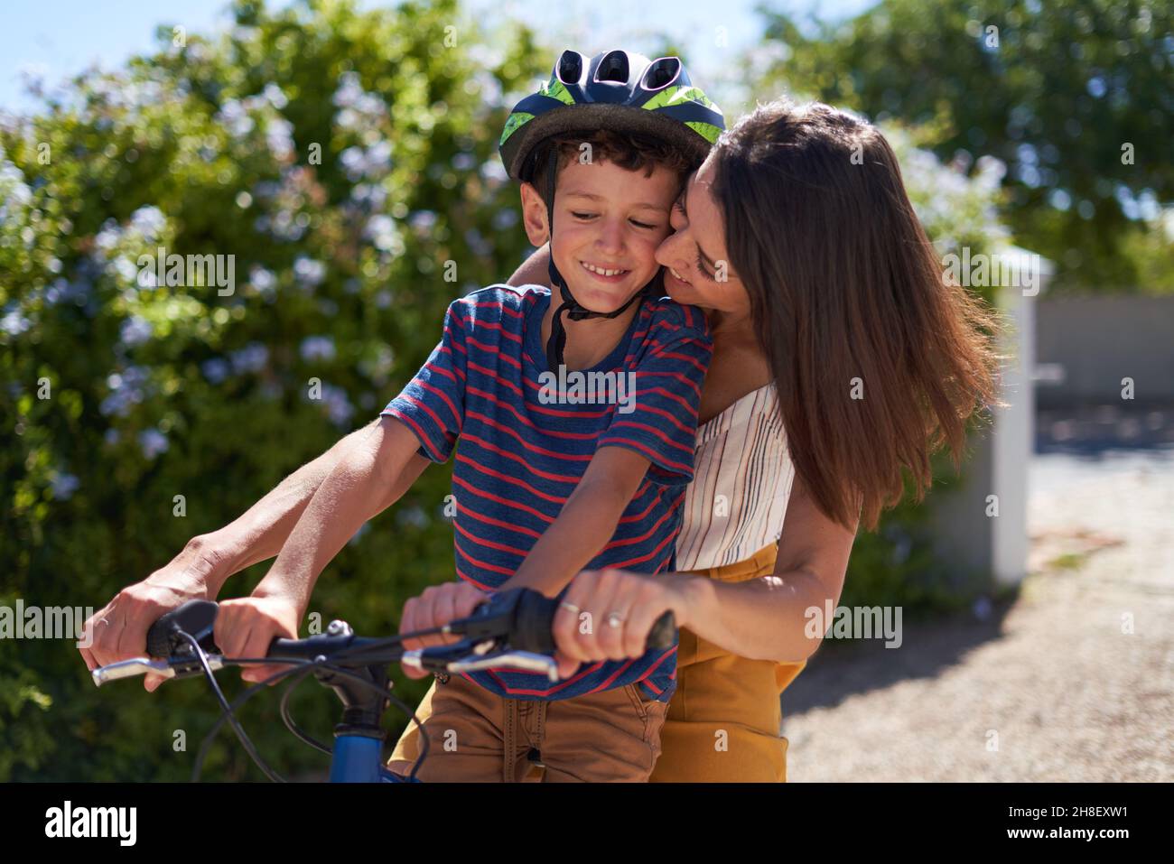 Felice affettuosa madre abbracciando figlio in bicicletta in strada soleggiata Foto Stock
