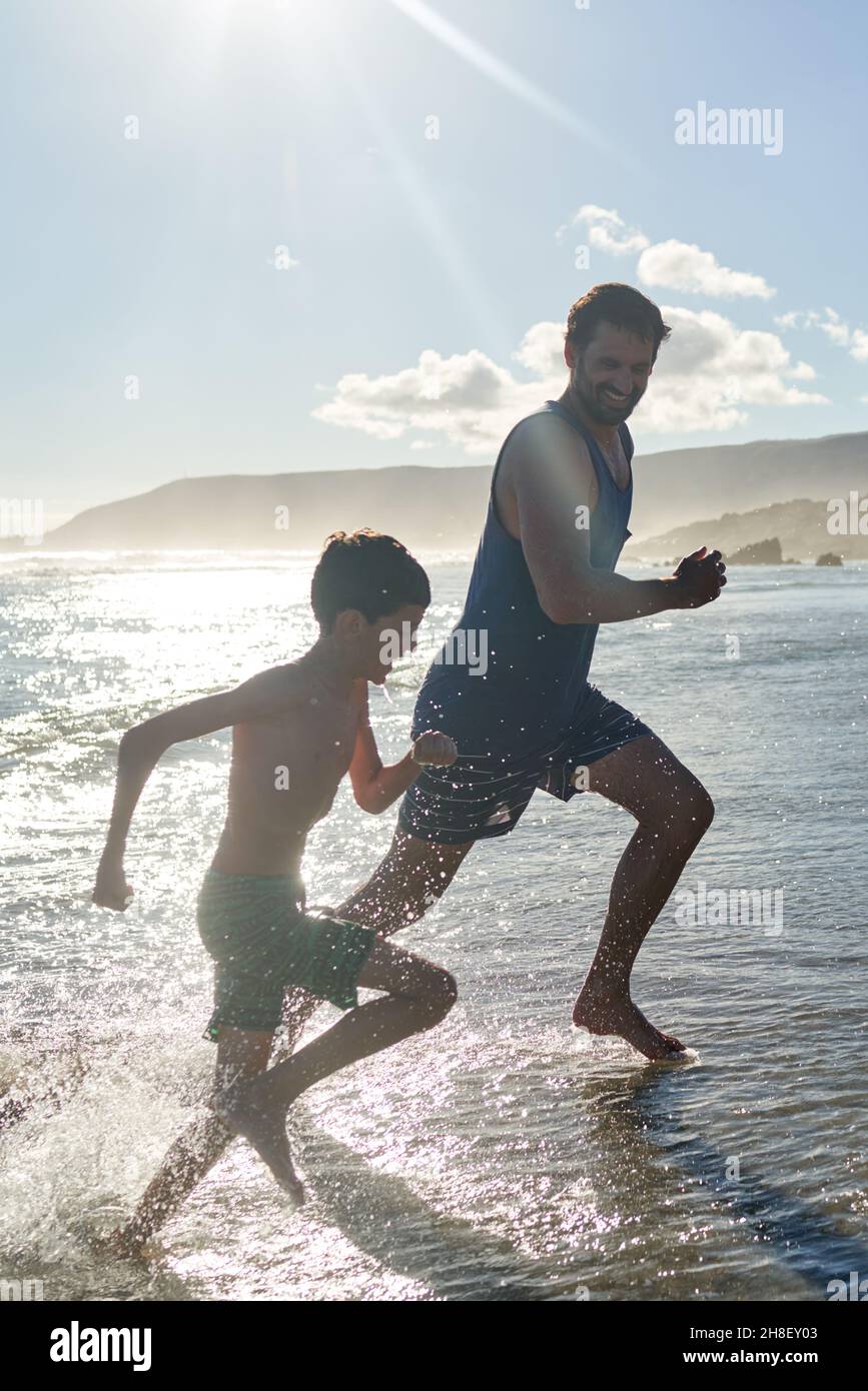 Felice padre e figlio che corre in estate soleggiato surf oceano Foto Stock