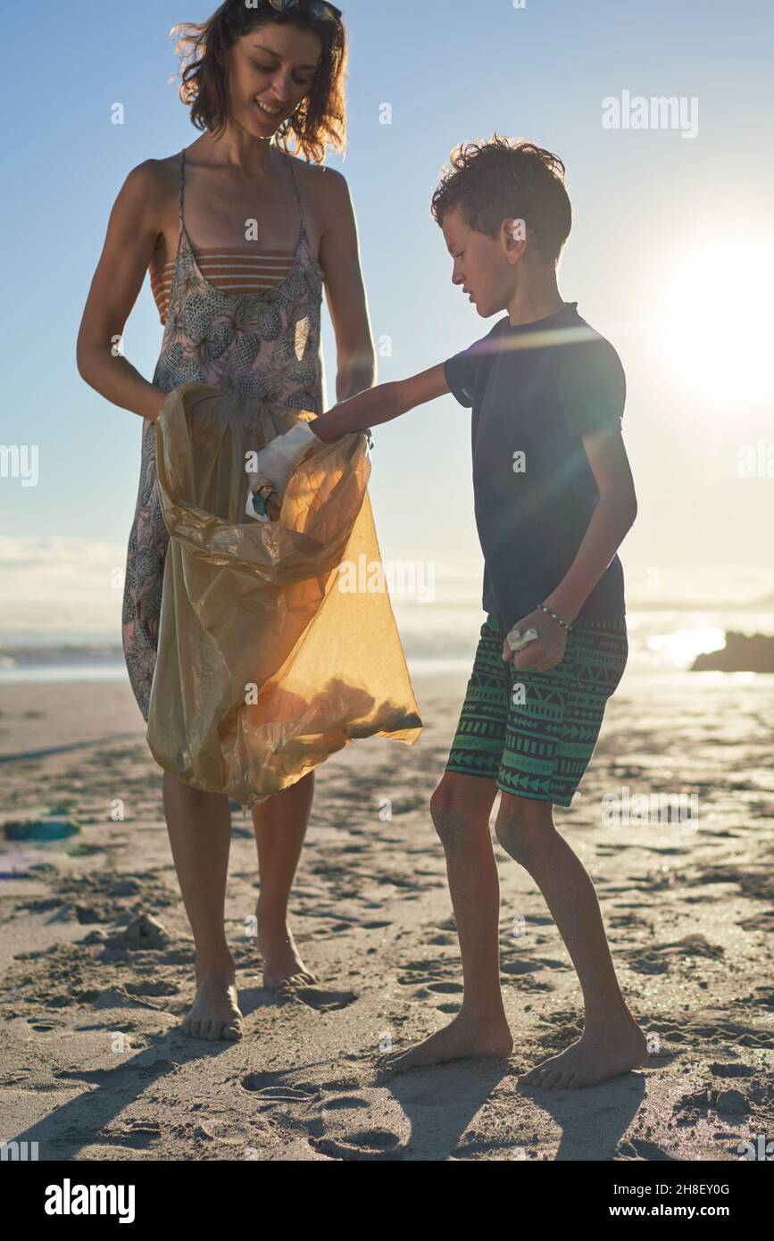 Madre e figlio che si dedicano al volontariato raccogliendo rifiuti sulla spiaggia soleggiata Foto Stock
