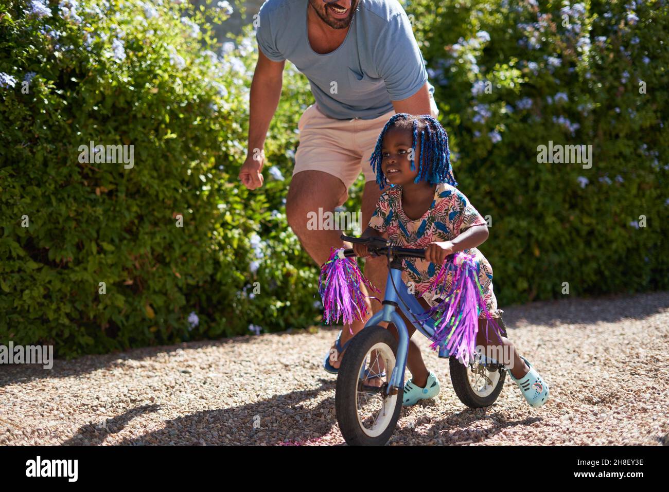 Papà aiutando la bambina in bicicletta in un vialetto soleggiato Foto Stock