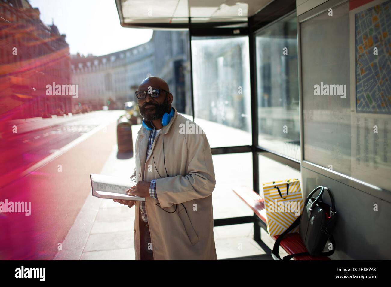 Uomo d'affari con libro in attesa alla fermata dell'autobus urbano, Londra, Regno Unito Foto Stock