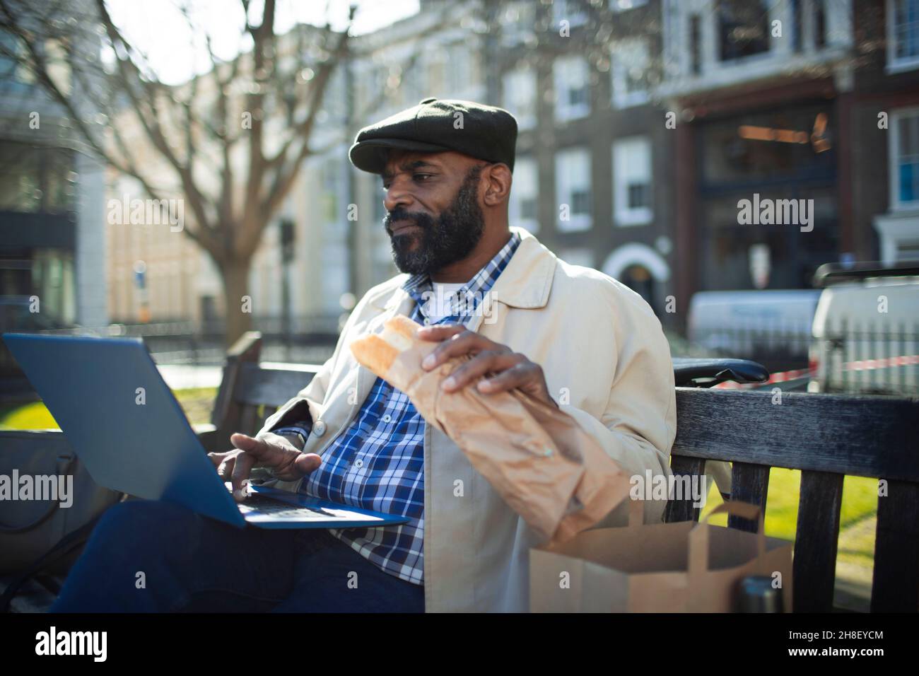 Uomo d'affari che mangia pranzo e lavora al computer portatile nel parco cittadino Foto Stock