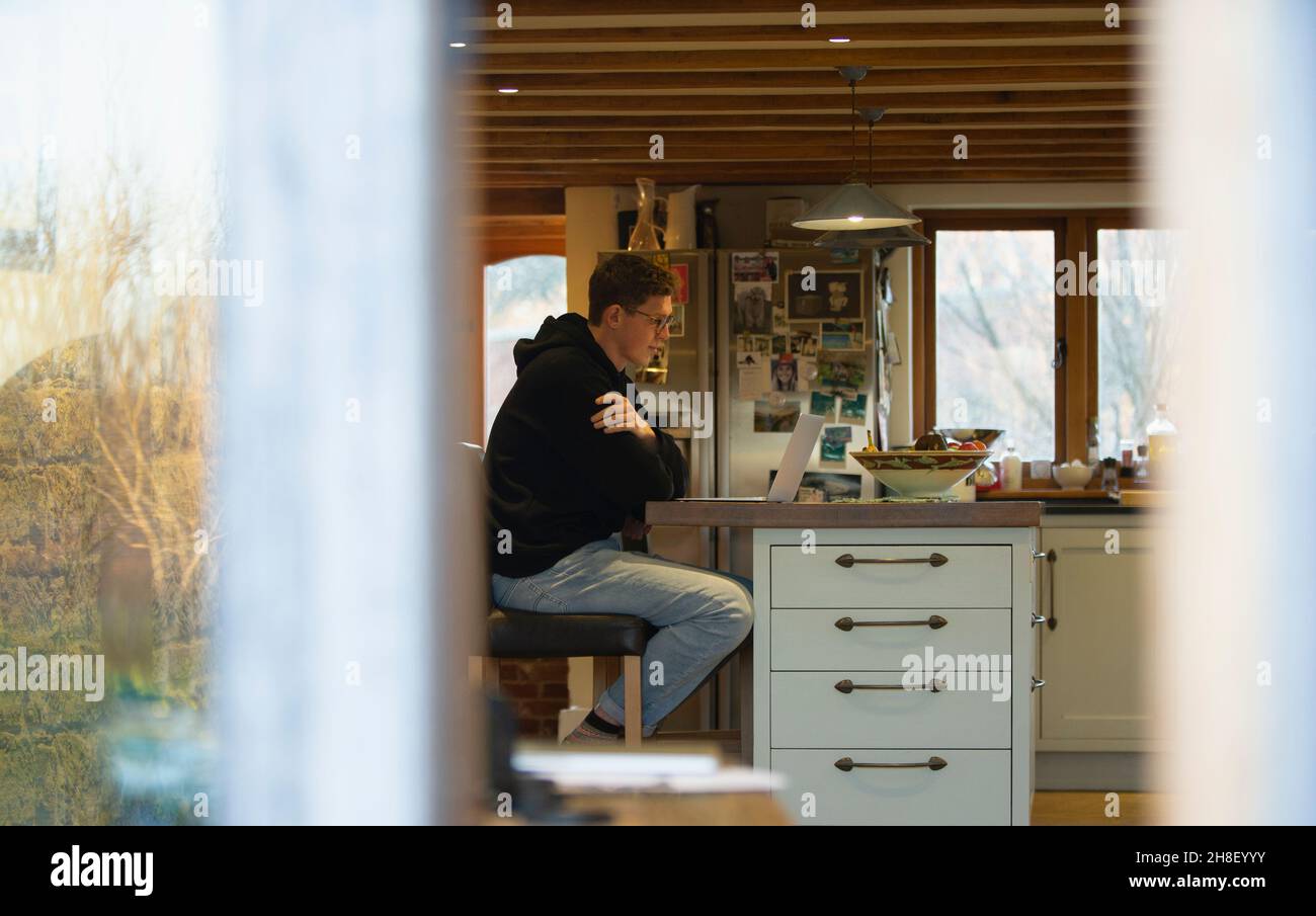 Uomo che lavora da casa al computer portatile sul banco della cucina Foto Stock