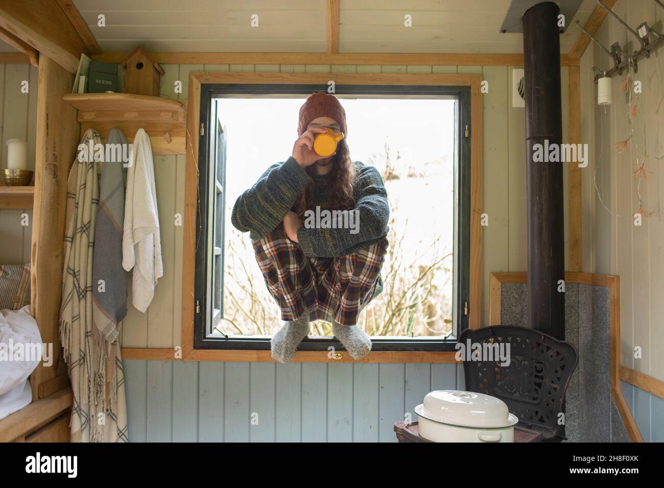 Giovane uomo in pigiama che beve caffè nella piccola finestra della cabina Foto Stock