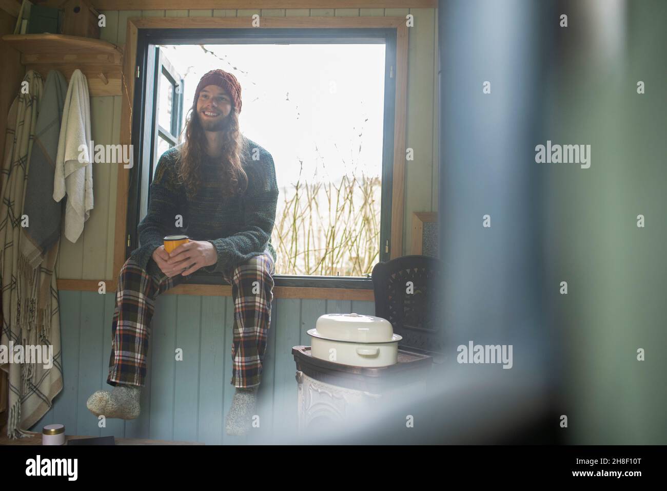 Buon giovane uomo in pigiama gustando caffè in cabina finestra Foto Stock