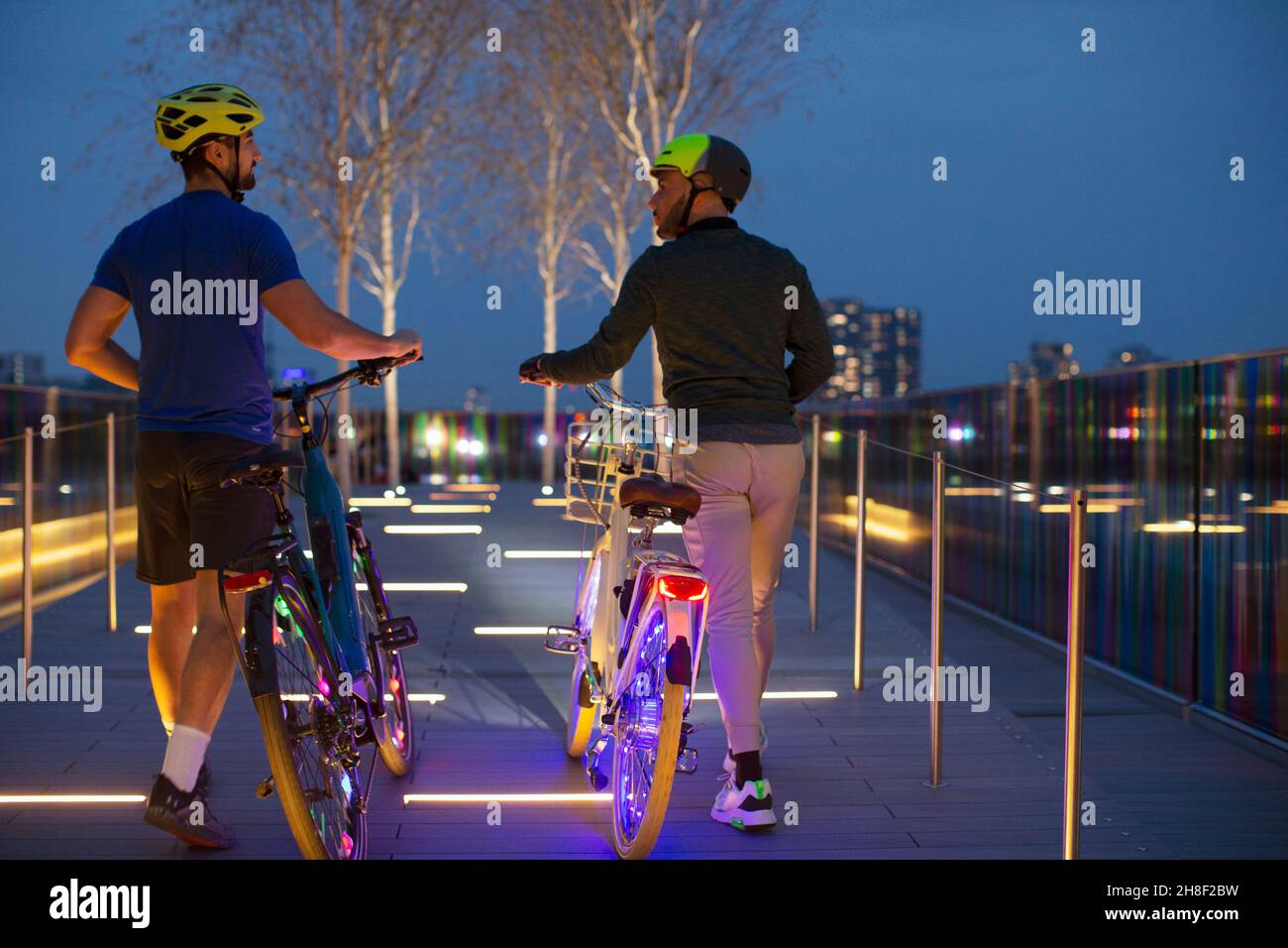 Uomini che camminano biciclette illuminate sul sentiero urbano, Londra, Regno Unito Foto Stock