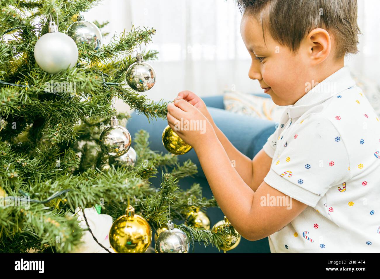 Ragazzo ispanico che mette una palla di Natale su un albero decorando per festeggiare Foto Stock