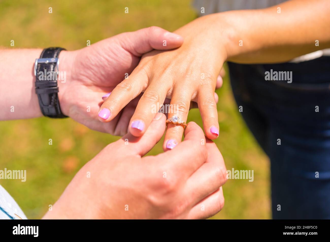 Primo piano di mani di due persone sconosciute in una proposta di matrimonio su uno sfondo sfocato erba Foto Stock