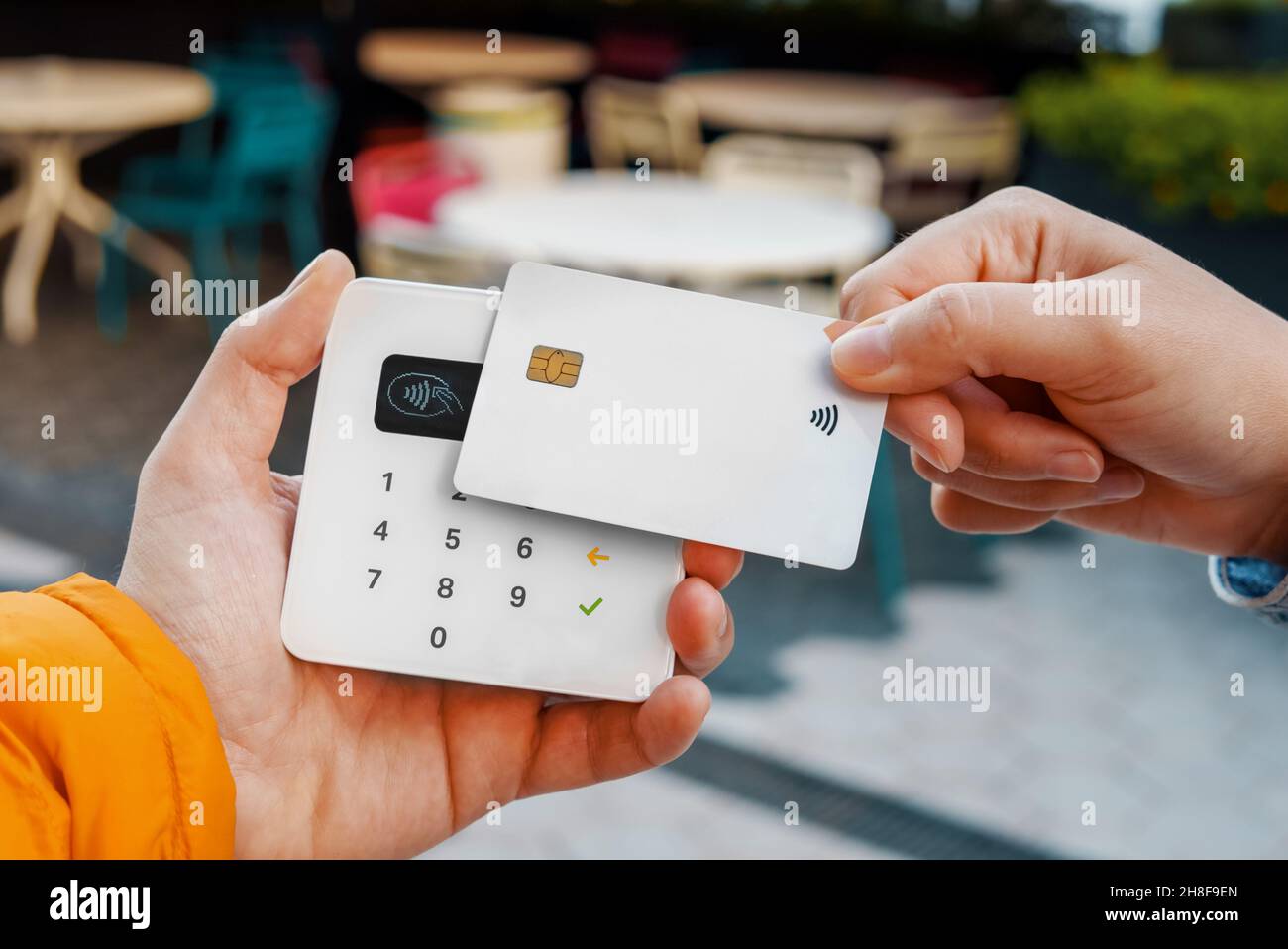 Alto angolo di raccolto anonima cliente che effettua il pagamento per l'ordine tramite carta di credito bianca utilizzando il terminale contactless in un bar all'aperto Foto Stock