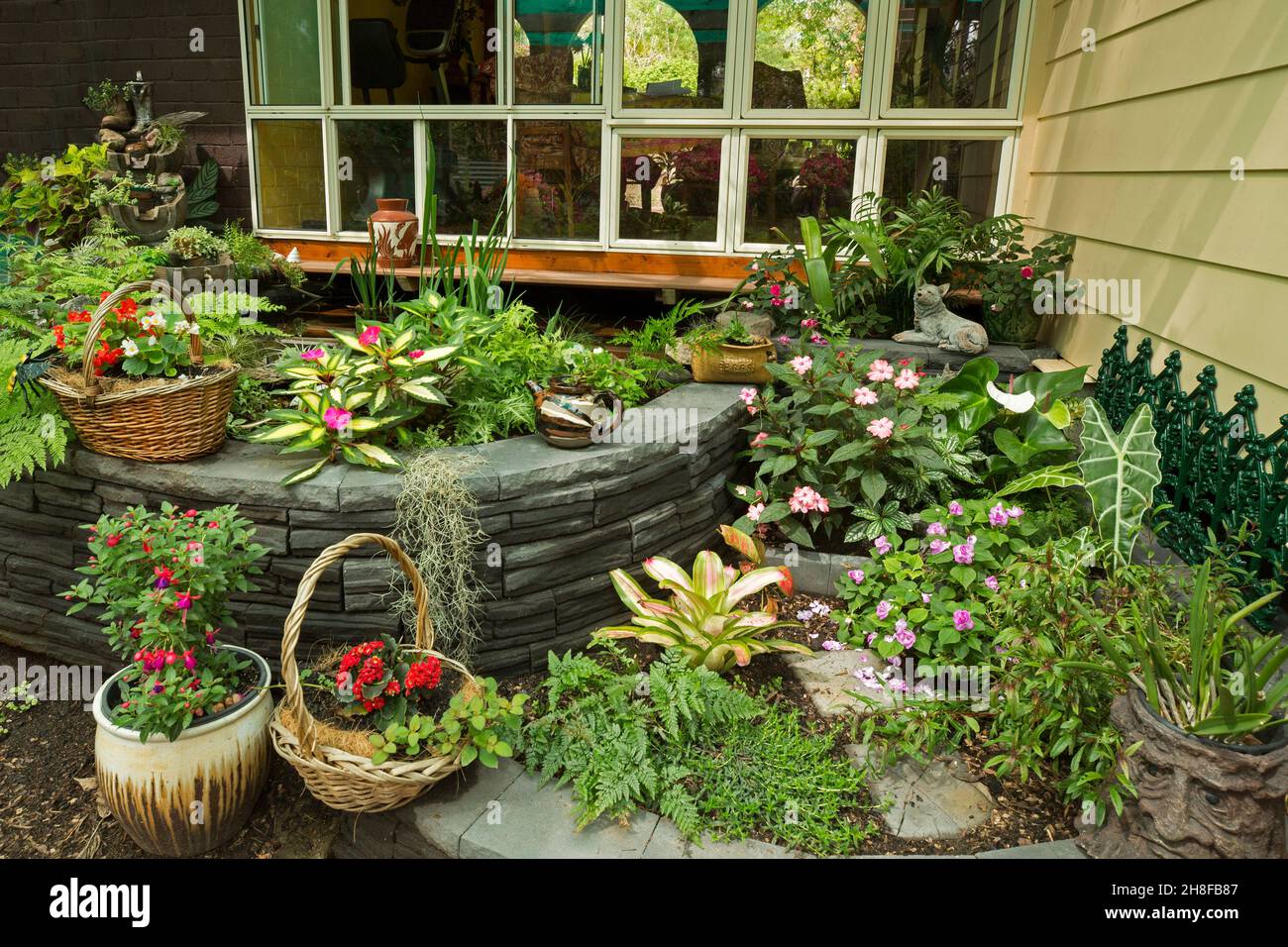 Spettacolare giardino cortile con pareti decorative e masse di fiori colorati, felci, piante con fogliame colorato, alcuni in contenitori ornati Foto Stock