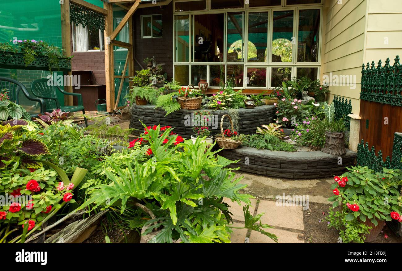 Spettacolare giardino coperto cortile con pareti decorative, ferro battuto e masse di fiori colorati, felci e piante con fogliame colorato Foto Stock