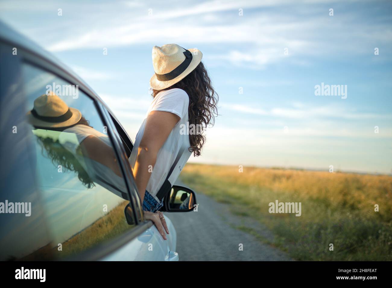 Giovane donna con cappello che attacca il suo corpo da un finestrino  dell'automobile. Libertà e concetto di avventura Foto stock - Alamy