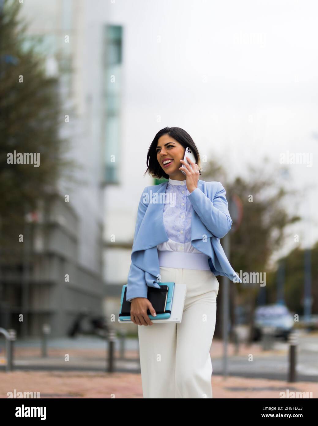Donna di successo che parla sul suo smartphone mentre cammina lungo la strada sorridendo Foto Stock