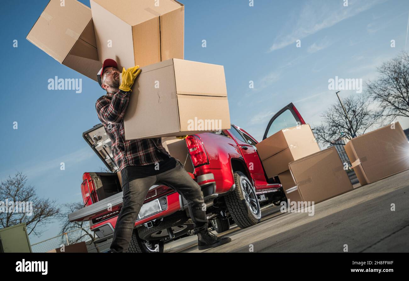 Caucasian Delivery Guy nei suoi 30s mobili scatole lungo. Alcune scatole cadono dalle sue mani quando cerca di ottenere troppi. Tema Courier. Foto Stock