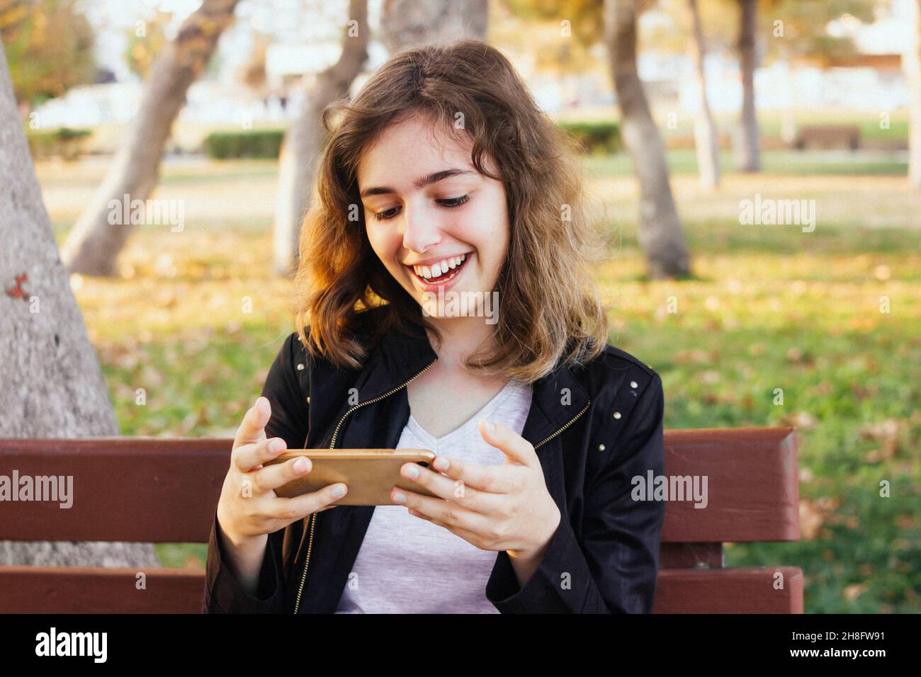 Ragazza sorridente felice che chiacchiera con gli amici tramite videochiamata sullo smartphone. Foto Stock