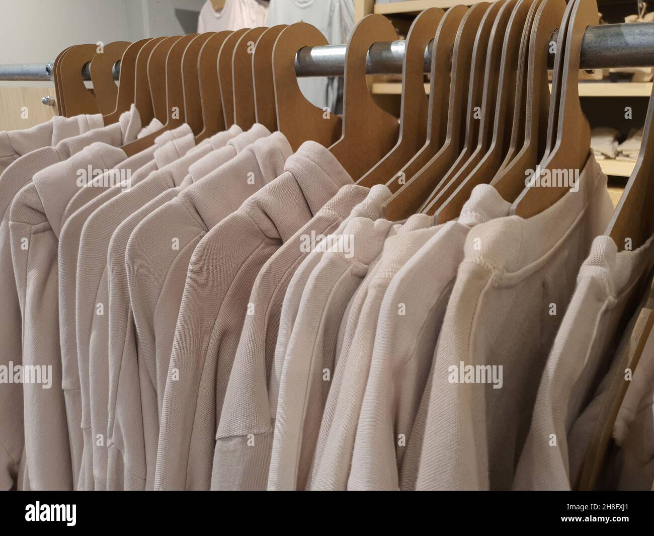 I vestiti casual si appendono su appendiabiti di carta di cartone eco-friendly in un negozio di abbigliamento in tonalità pastello alla moda e di colore beige. Concetto di abbigliamento senza sesso. Messa a fuoco selettiva Foto Stock