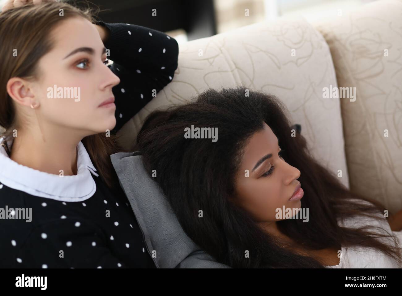 La donna brunetta e la sua amica latino americana guardano la televisione a casa sul divano Foto Stock