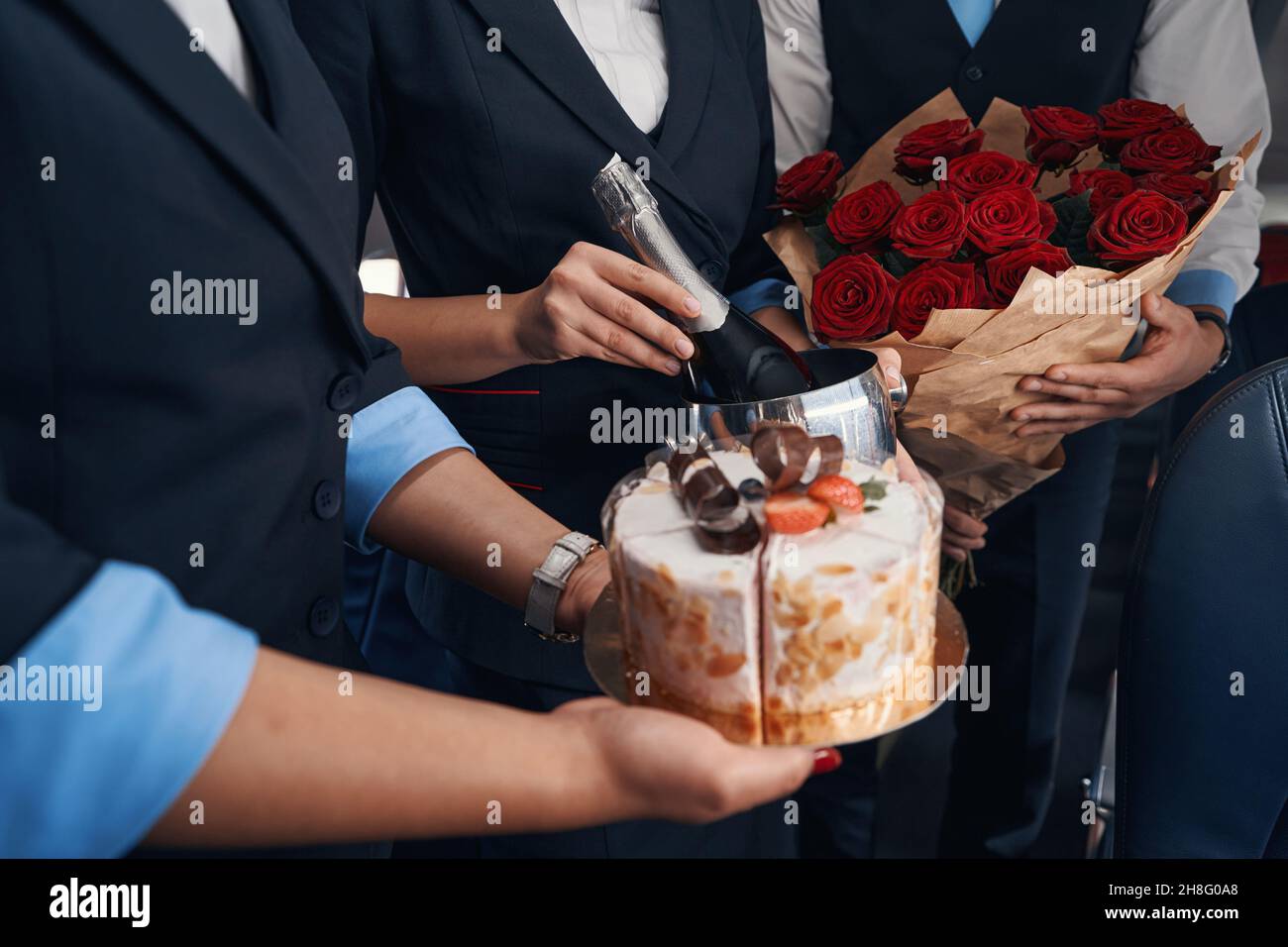 Torta, bottiglia di champagne e fiori in mano dell'equipaggio di cabina Foto Stock