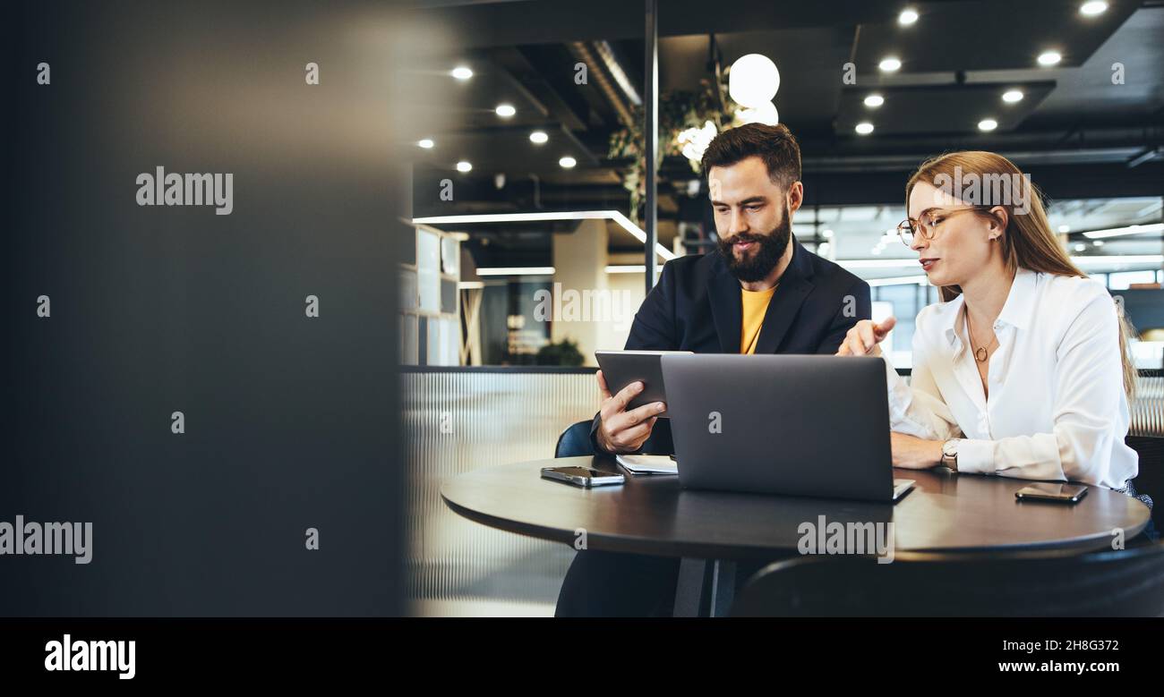 Due giovani imprenditori che utilizzano un tablet digitale mentre discutano in un ambiente di lavoro moderno. Due giovani uomini d'affari che utilizzano la tecnologia wireless Foto Stock