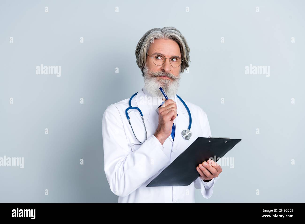 Foto di dubbioso uomo anziano doc vestito bianco uniforme occhiali scrivere prescrizioni cercando spazio vuoto isolato grigio sfondo di colore Foto Stock