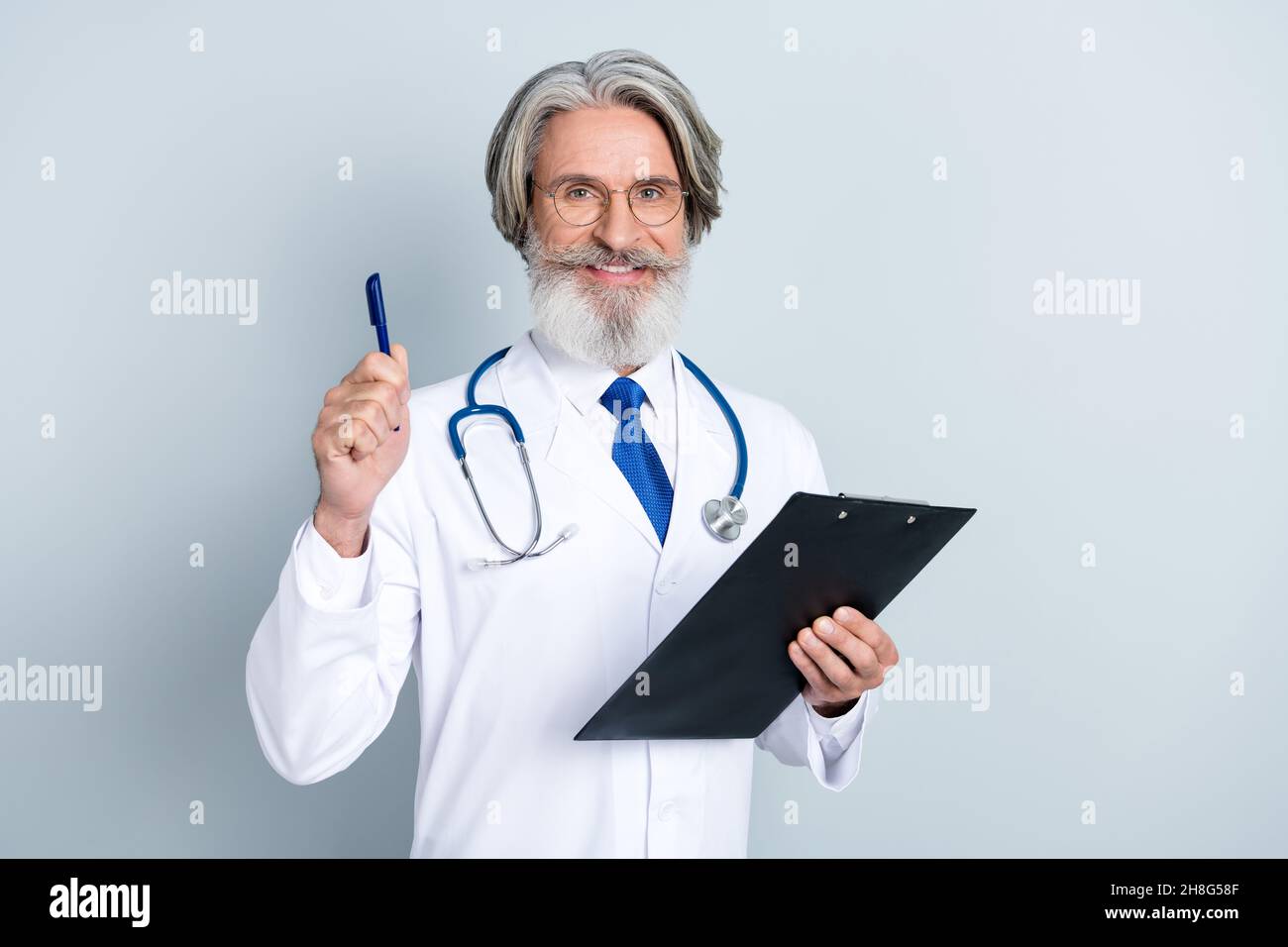 Foto di astuto uomo anziano doc vestito bianco uniforme occhiali scrittura prescrizioni puntando penna isolato grigio sfondo di colore Foto Stock
