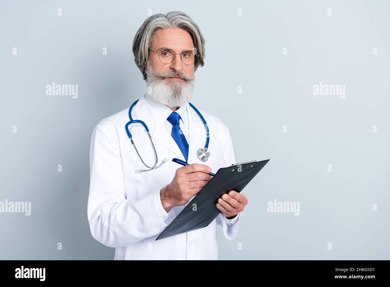Foto di bravo uomo anziano serio doc vestito bianco uniforme occhiali scrittura prescrizioni spazio vuoto isolato grigio sfondo di colore Foto Stock