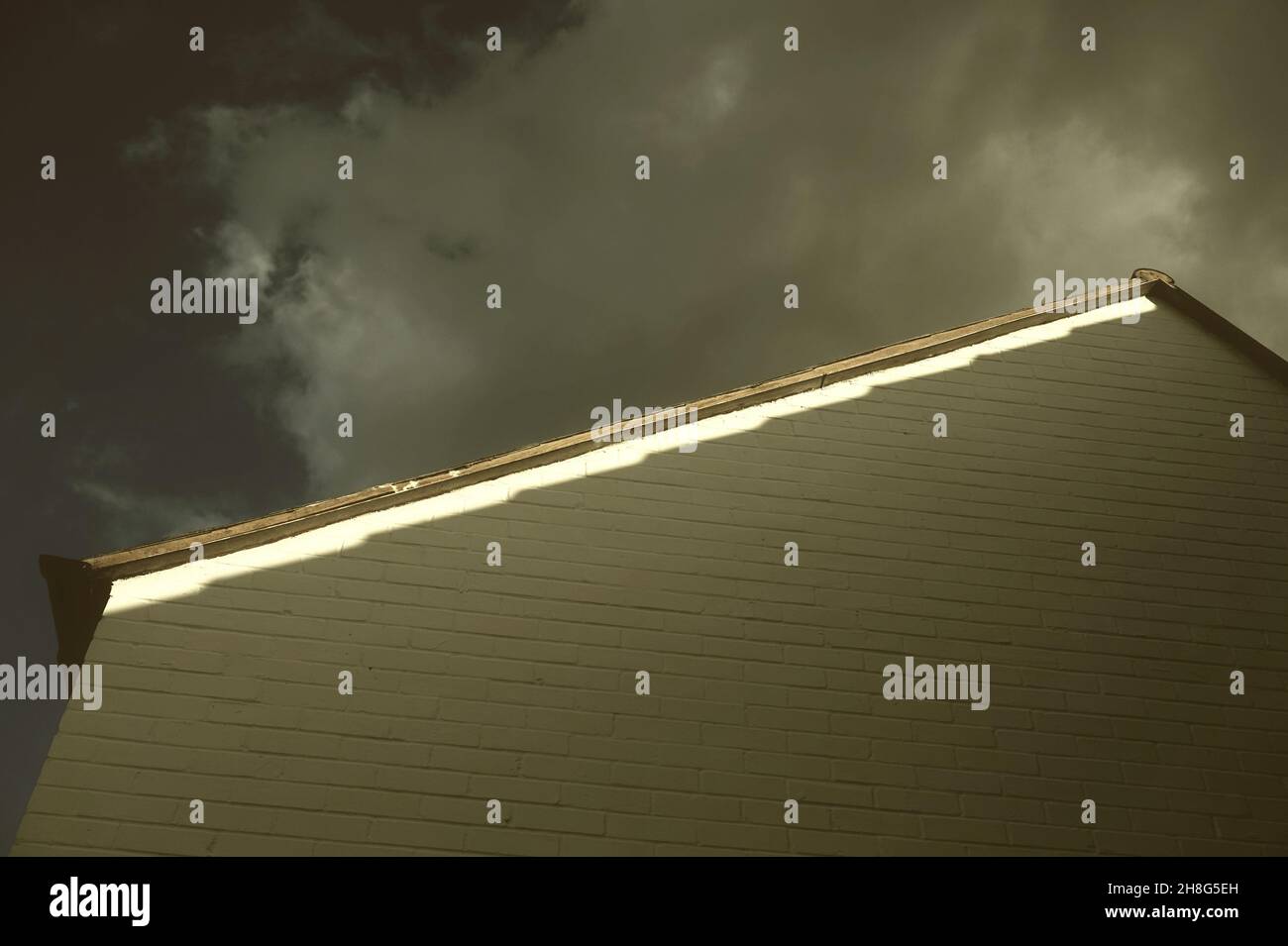 Una sottile linea di luce solare colpisce il tetto di un edificio mentre una tempesta si avvicina a Londra, Regno Unito Foto Stock