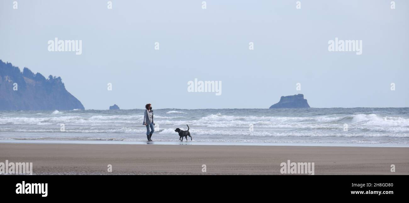 Donna che cammina un cane su Cannon Beach, Oregon Foto Stock