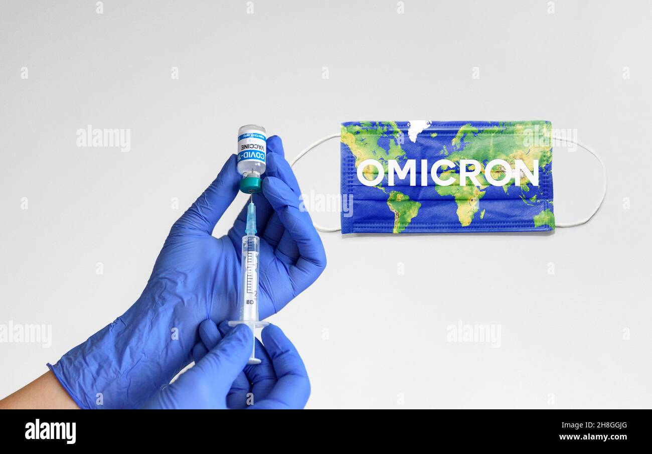 Operatore medico con guanti blu che tengono la siringa del flaconcino di vaccino del coronavirus di fronte a sfondo bianco con testo omicron sulla maschera facciale Foto Stock