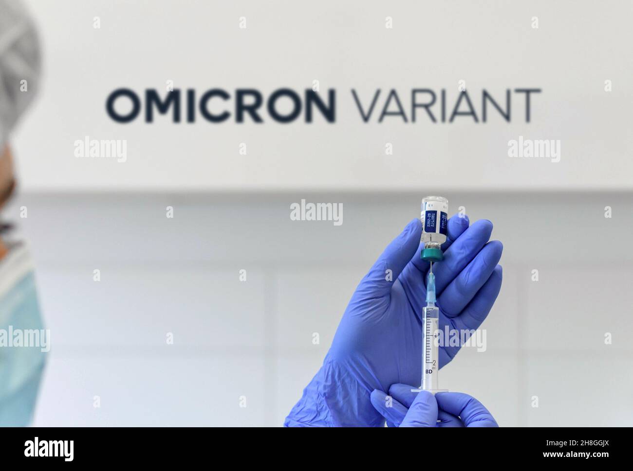 Operatore medico con guanti bianchi che tengono la siringa del flaconcino di vaccino del coronavirus di fronte a sfondo bianco con il testo omicron e l'icona del virus Foto Stock