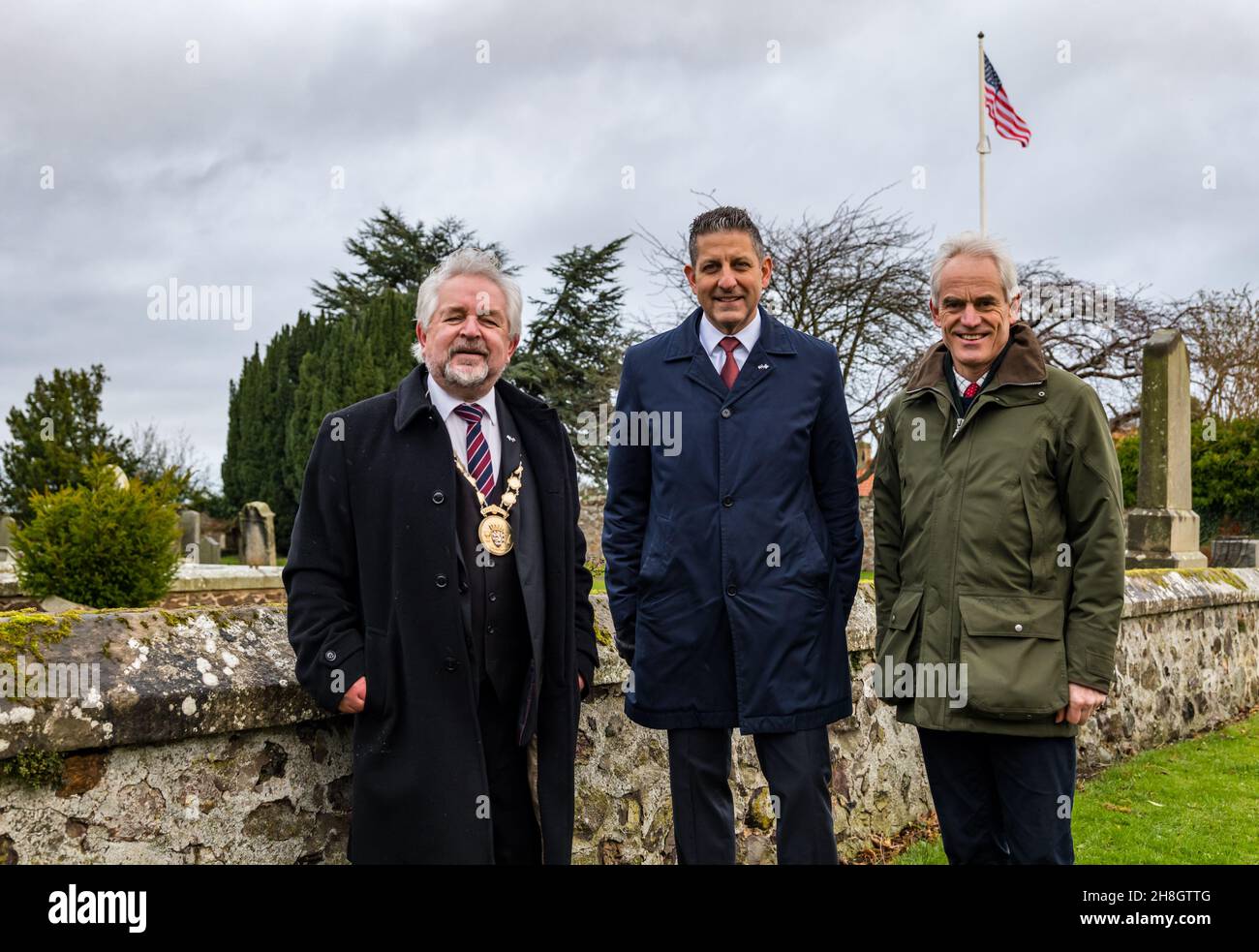 Athestaneford, East Lothian, Scozia, Regno Unito, 30 novembre 2021. Il Consolato GENERALE DEGLI STATI UNITI presso lo Scottish Flat Trust il giorno di St Andrew: Jack Hillmeyer del Consolato degli Stati Uniti Edimburgo è benvenuto per celebrare il giorno di St Andrew al luogo di nascita del Saltyre in un tipico giorno scozzese da sogno. Una bandiera degli Stati Uniti è sollevata in suo onore nel cortile del villaggio. Nella foto: Jon McMillan (Provost of East Lothian), Jack Hillmeyer, Console Generale degli Stati Uniti e Roderick Urquhart (Lord Lieutenant of East Lothian) Foto Stock