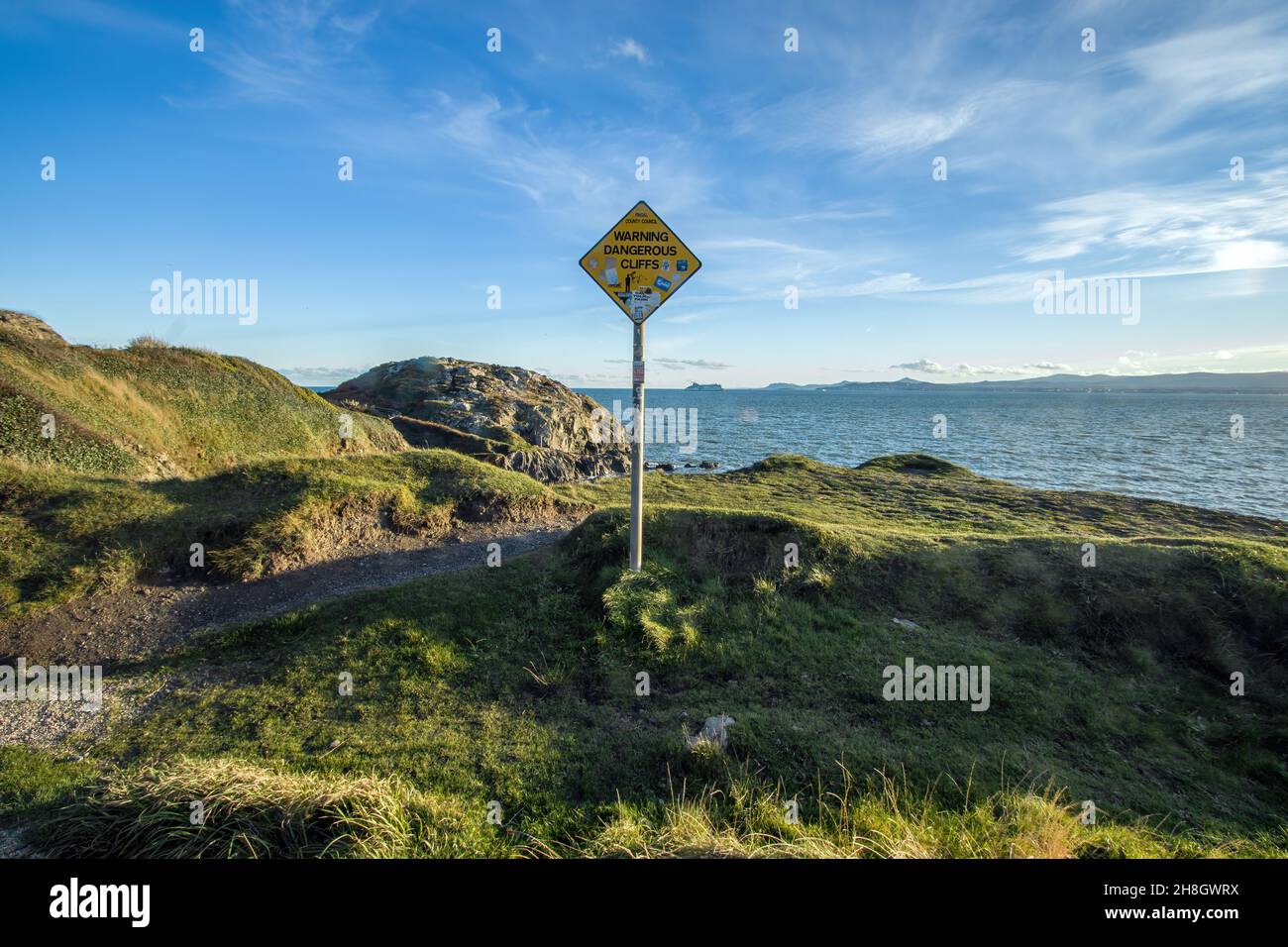 Avvertimento e informazioni segno sul sentiero della penisola di Howth testa in bella giornata di sole, in ombra e riflessi d'acqua Dublino, Irlanda Foto Stock