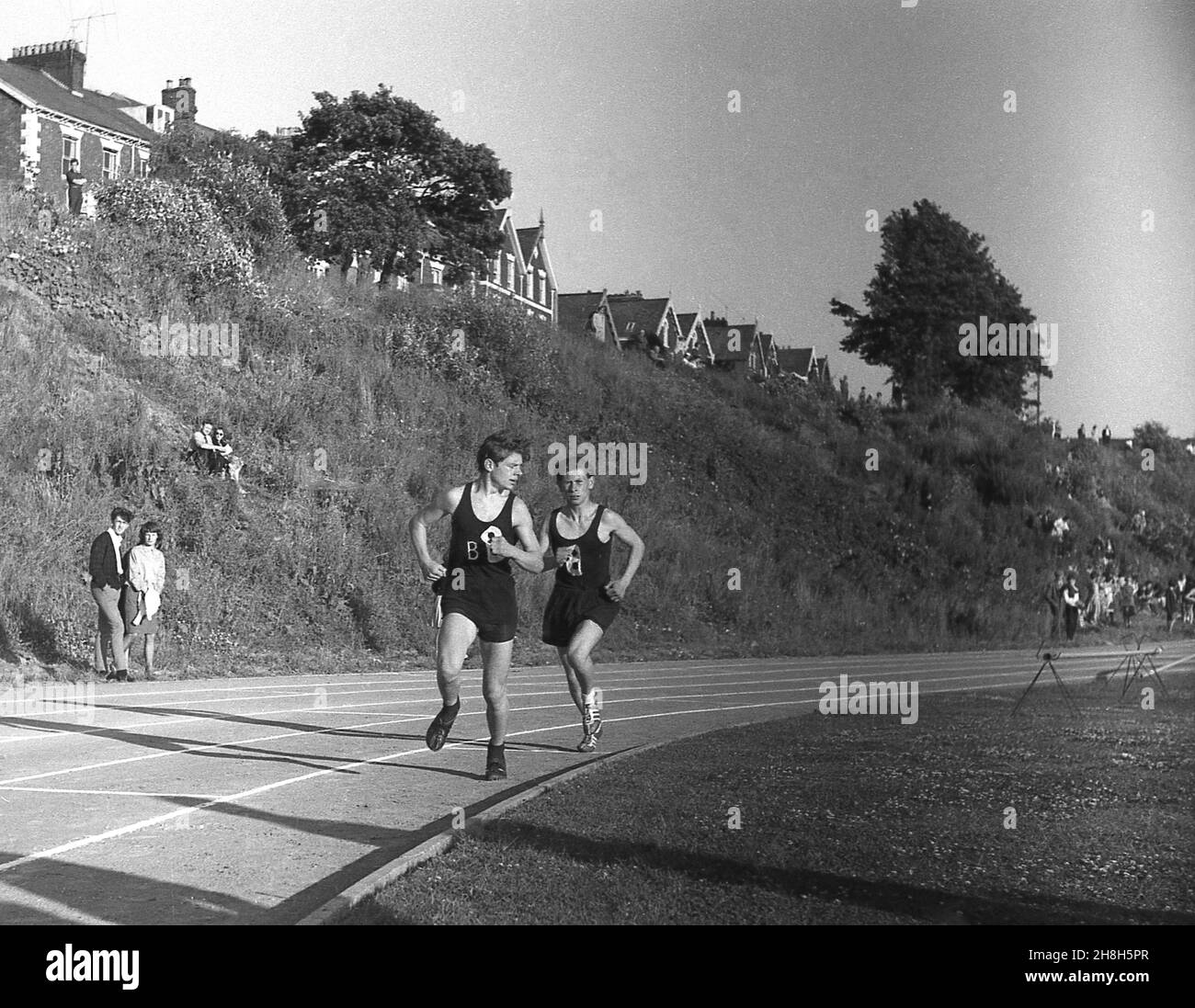 1964, storico, estivo ed esterno su una pista di cinder, due ragazzi adolescenti che gareggiano in una gara di corsa ad una giornata sportiva della scuola della contea, Devon, Inghilterra, Regno Unito. Foto Stock